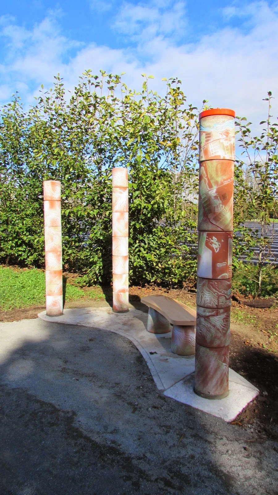 Three terracotta wayfinder columns and a curved seat at the Point Wells end of the walkway