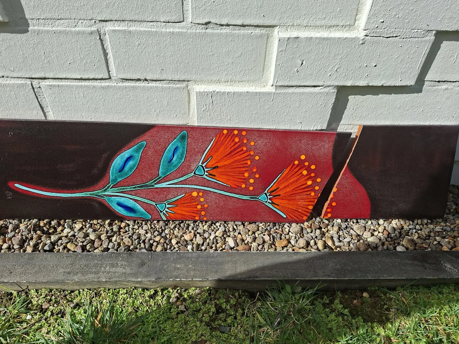 A red Pōhutukawa wall panel broken into pieces, leaning against a brick wall