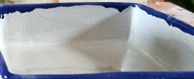 Close up of a white glazed dish with a blue rim, showing a fine network of crazing lines