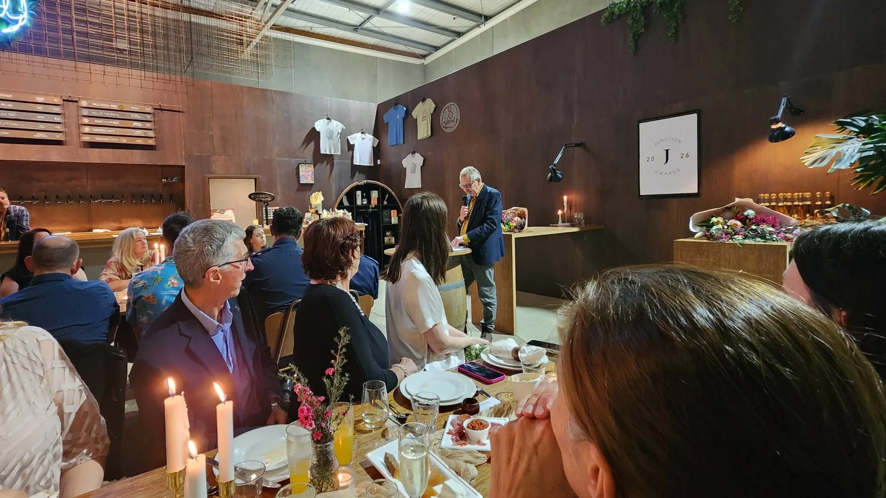 Kieran Rice giving the keynote at the Junction Awards 2026, with guests seated at candlelit tables