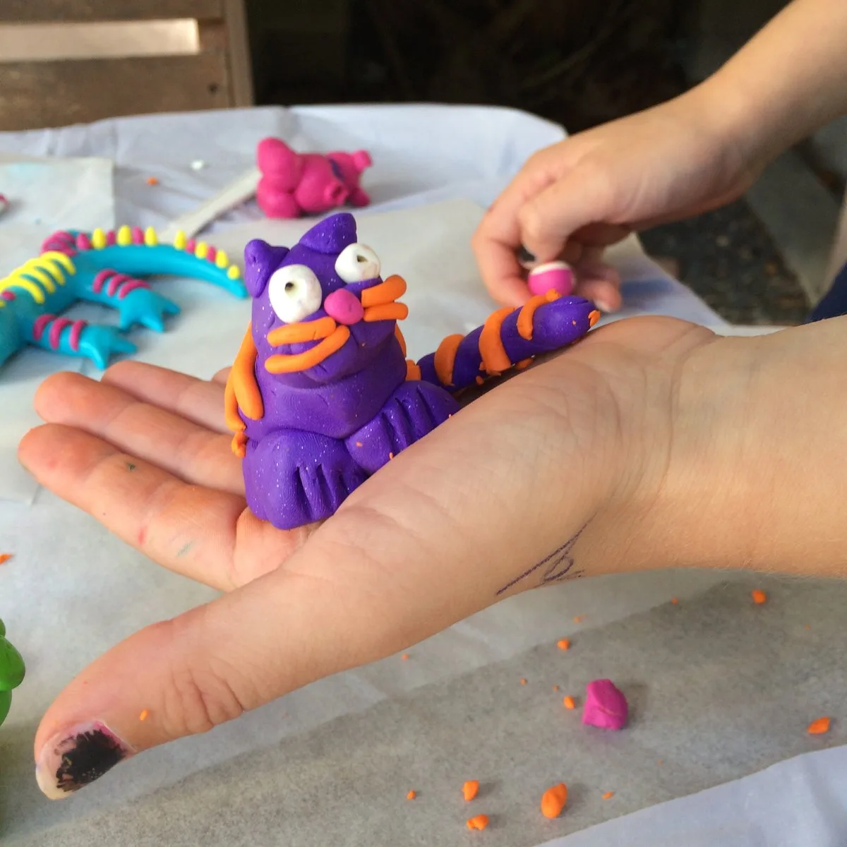 A purple and orange clay cat on a child’s hand