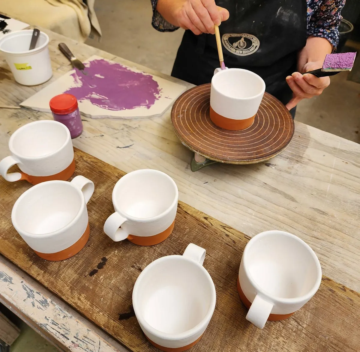 A decorator in a Morris & James apron painting purple onto a row of white and terracotta mugs