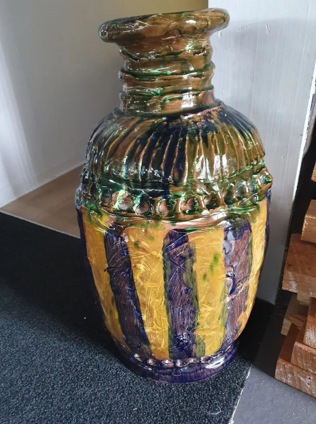 A tall textured jar by Ant Morris with a coiled neck, green and brown glaze on the shoulder, and yellow and cobalt stripes