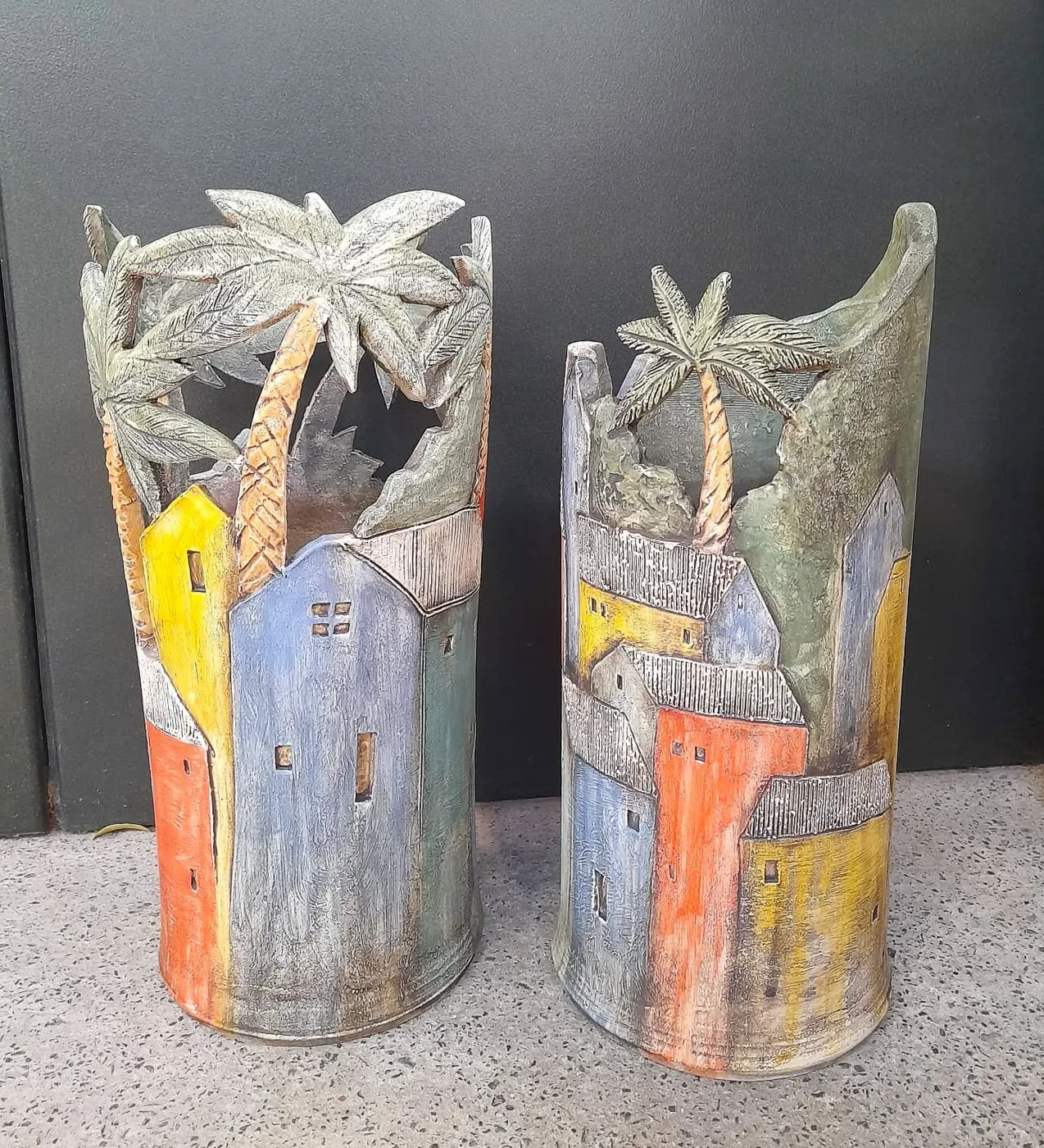 Two tall vessels by Nick Charlton, carved with colourful houses and palm trees
