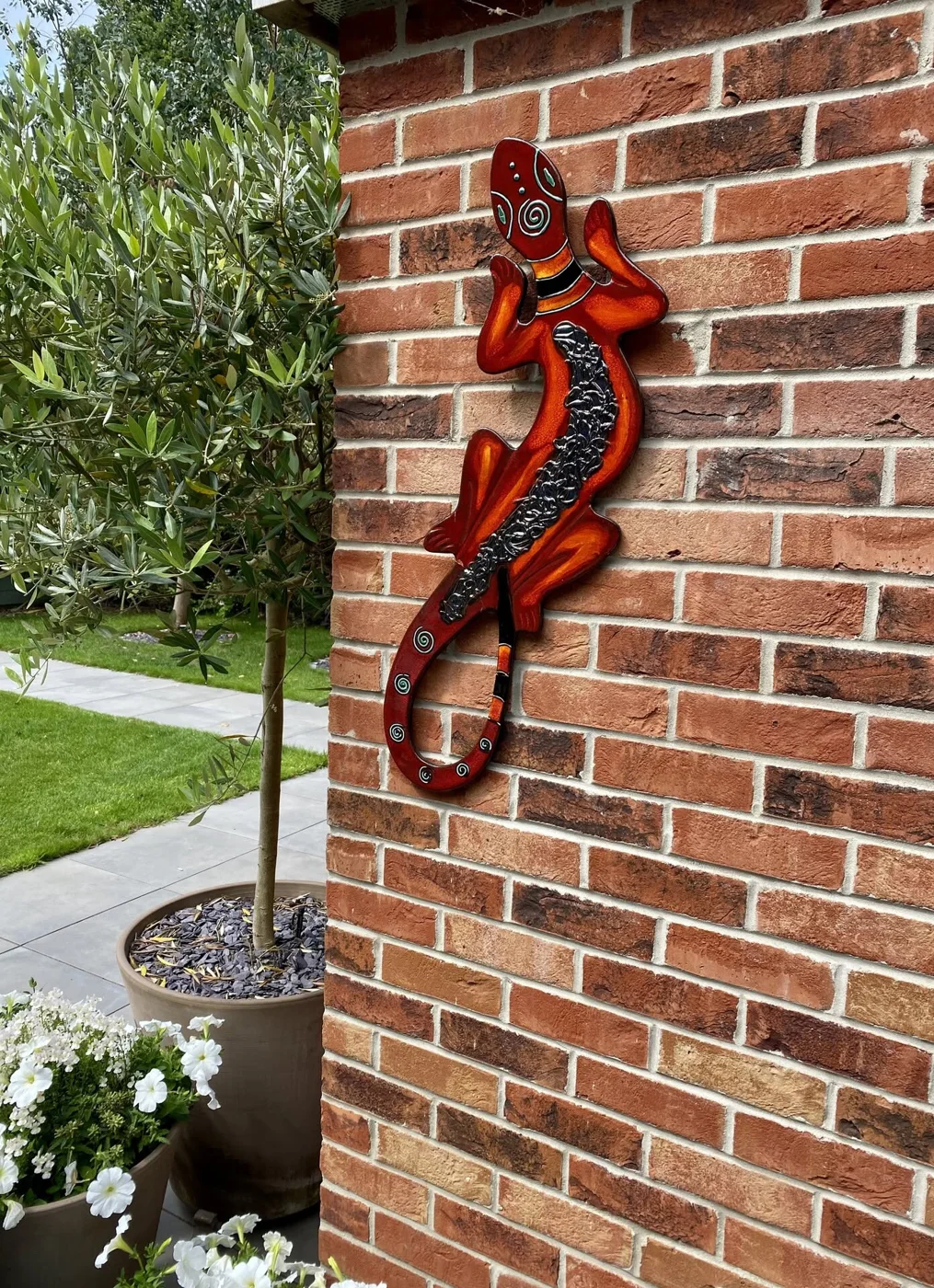 A large red and orange lizard wall follie with a silver-glazed back, on a brick wall