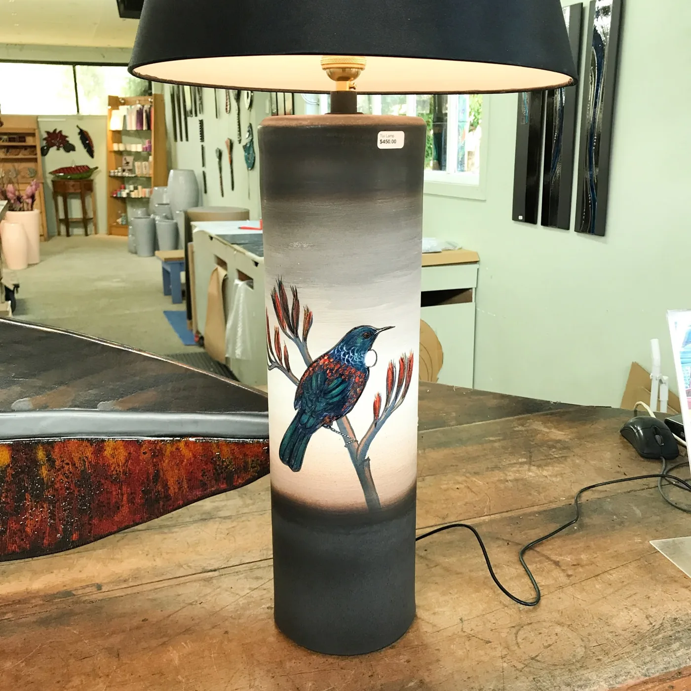 A tall lamp base hand-painted with a tūī on flax flowers, with a black shade