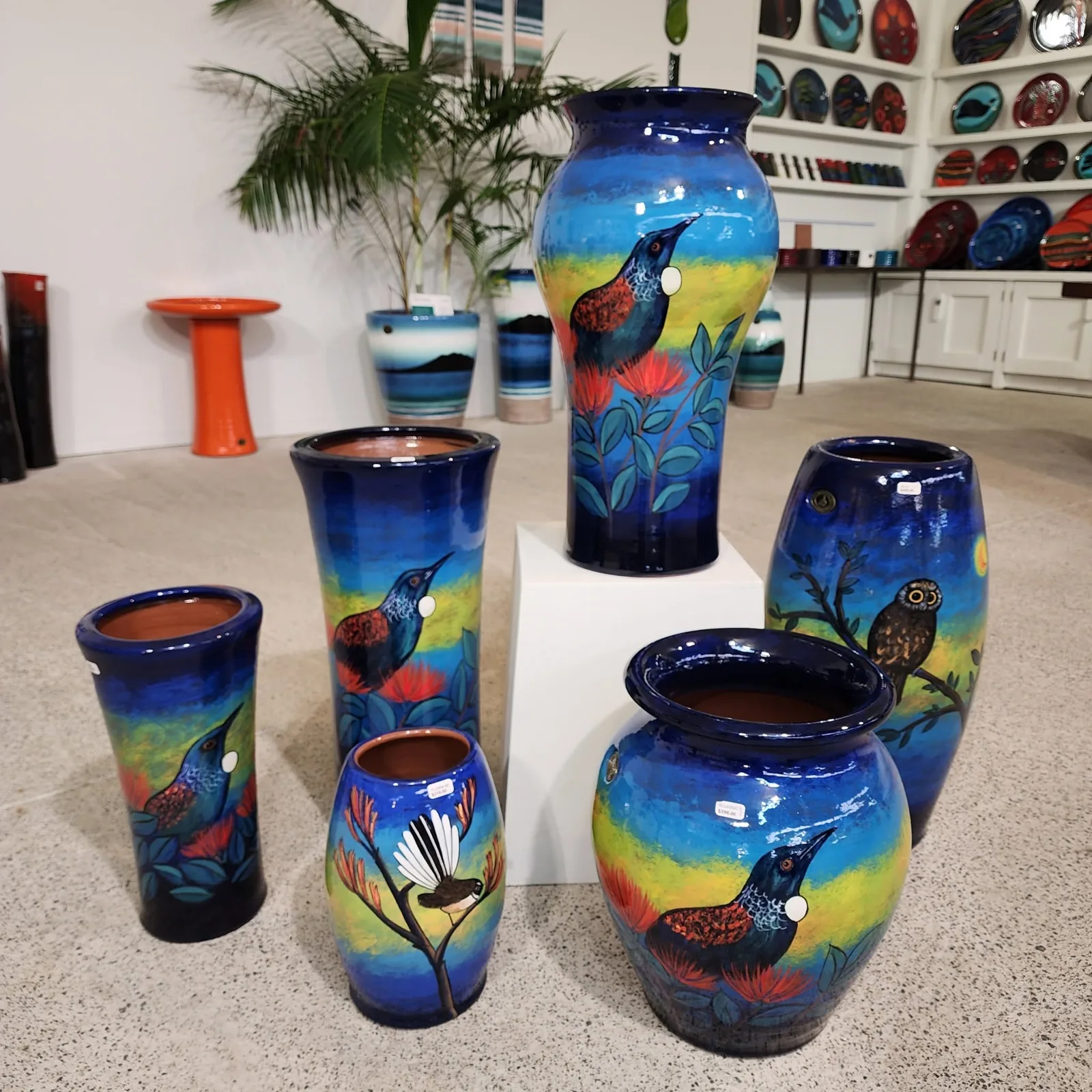 Pots hand-painted with tūī, a fantail and a ruru on deep blue glaze
